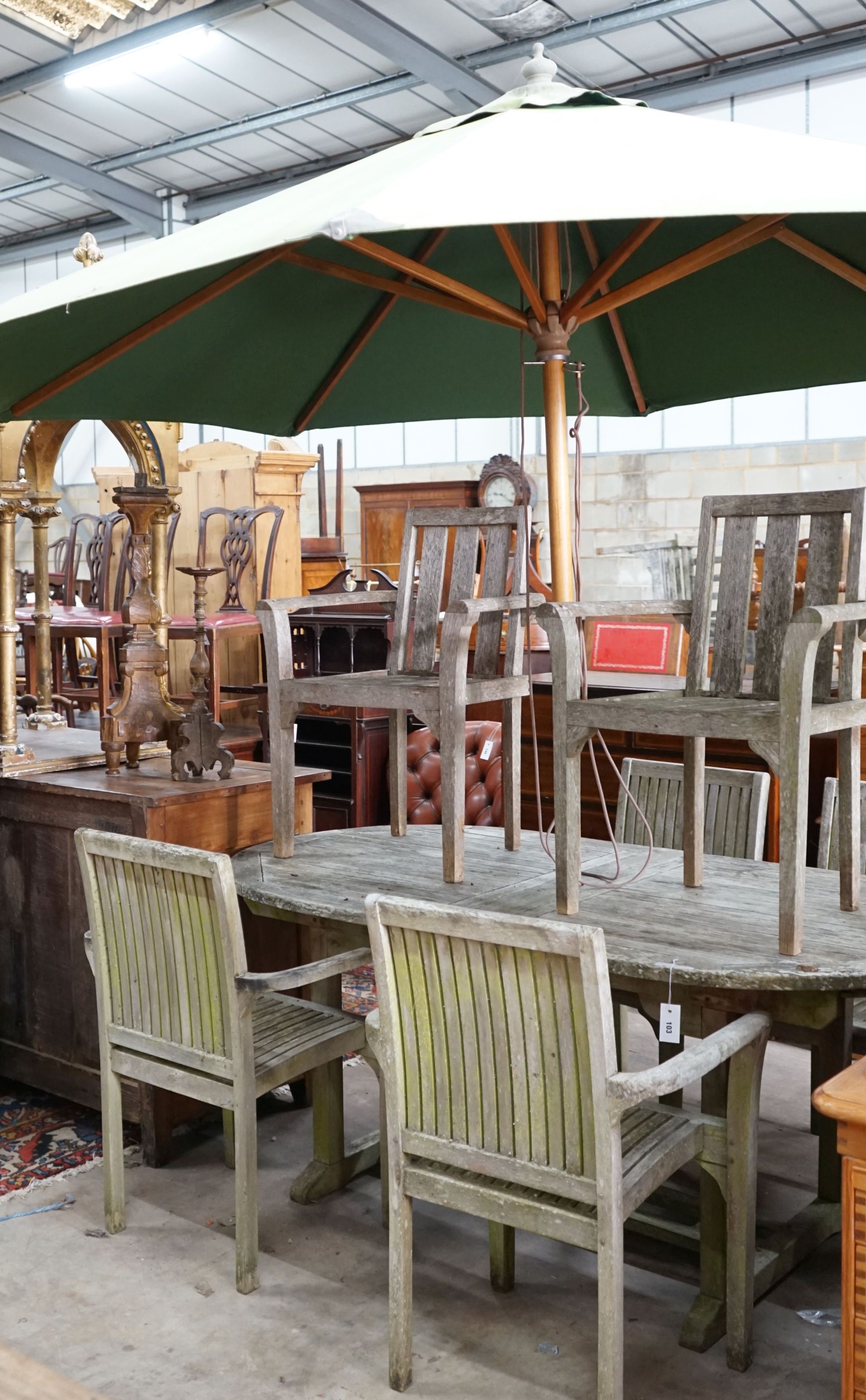 An oval weathered teak extending garden table, length 180cm, depth 100cm, height 76cm with six elbow chairs (4+2) and green canvas crank parasol